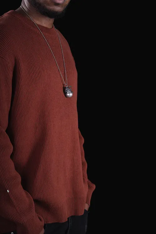 A man wearing a pendant necklace over a rust-coloured knitted top