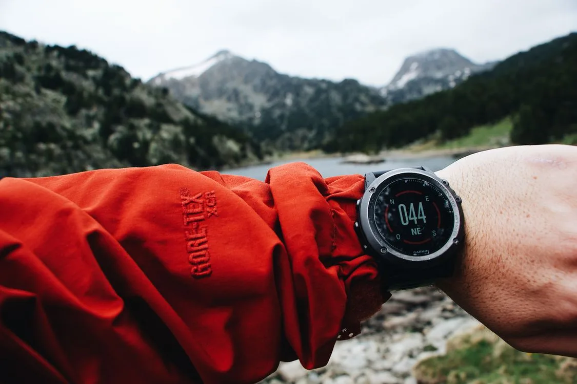 A wristwatch worn with an outdoor jacket beside a mountain lake